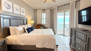 A hotel room with a bed, a TV, a ceiling fan, a chair, and a view of the ocean.