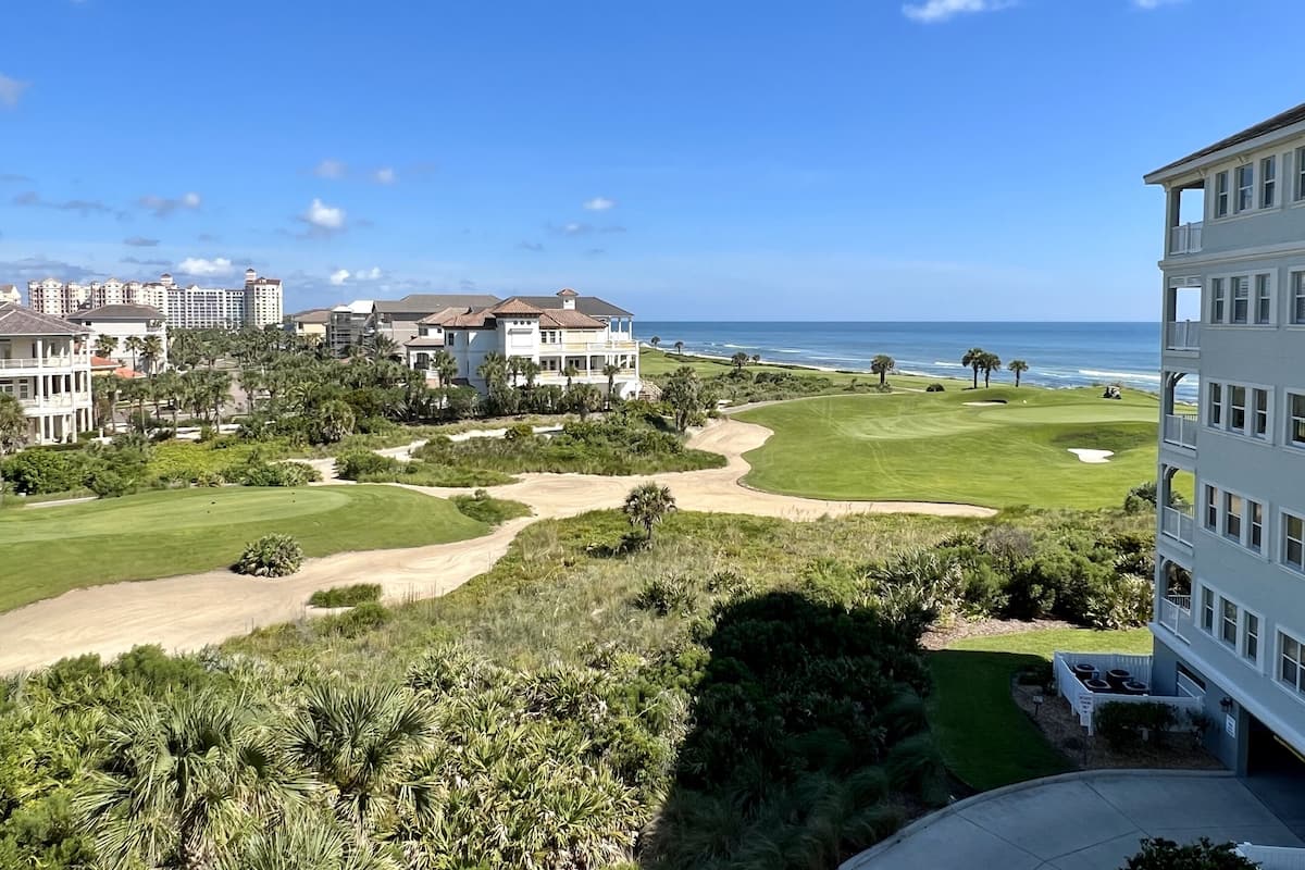 A golf course with a view of the ocean and a large building with multiple stories.