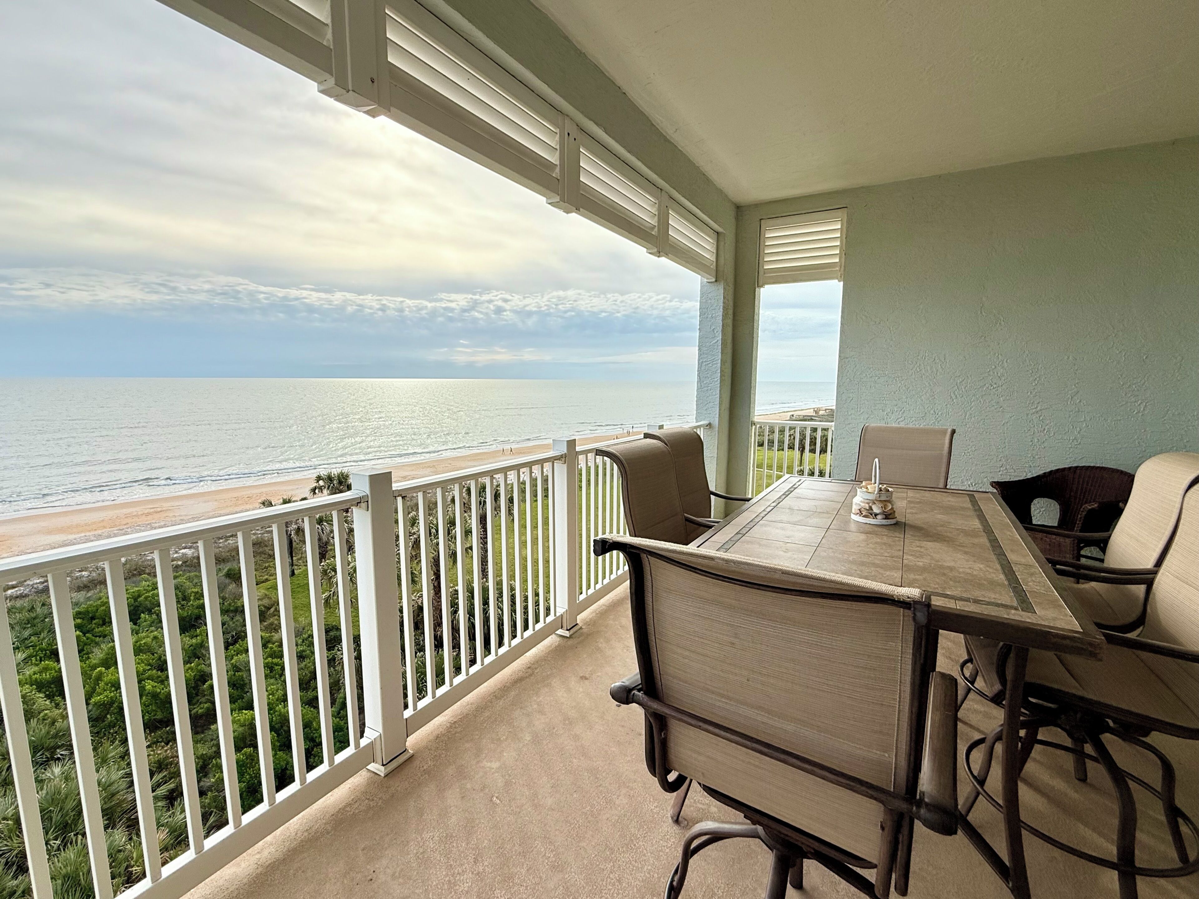 A balcony with a view of the ocean, a table with chairs, and a railing.