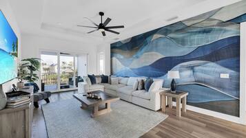 A spacious living room with a large abstract mural, a ceiling fan, and a view through the glass doors.