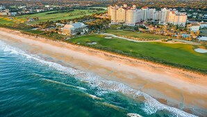 Vista aérea de un complejo turístico costero con campo de golf, playa y varios hoteles de gran altura.