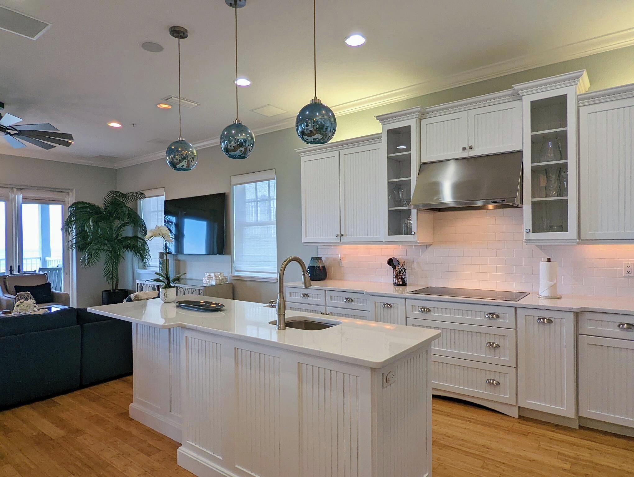 Una cocina moderna con armarios blancos, una isla central, luces colgantes y un amplio ventanal.