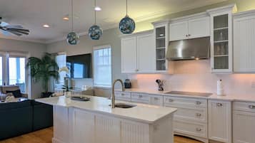 Una cocina moderna con armarios blancos, una isla central, luces colgantes y un amplio ventanal.