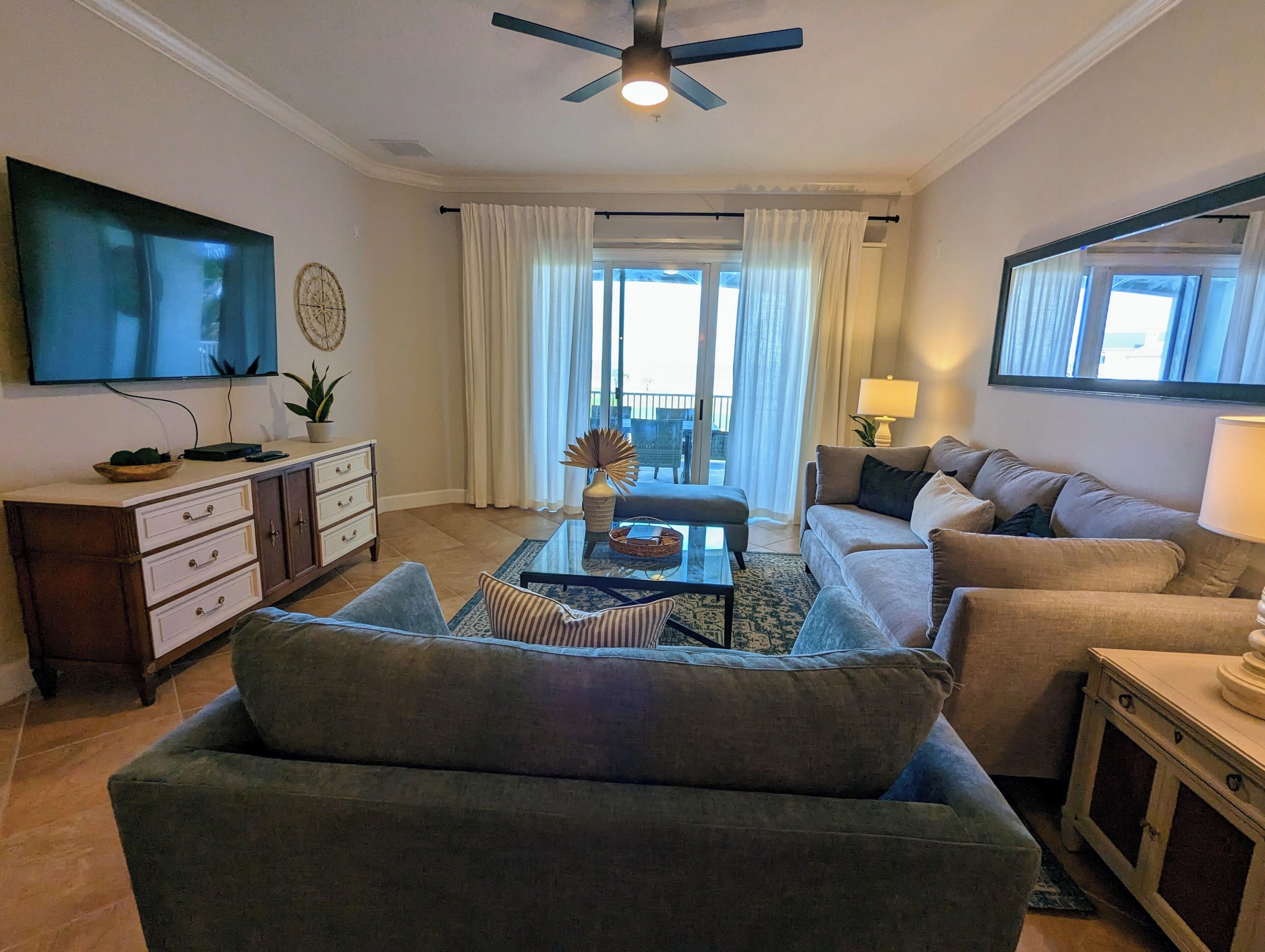 Un salon avec un canapé, une table basse, un téléviseur et un ventilateur de plafond.
