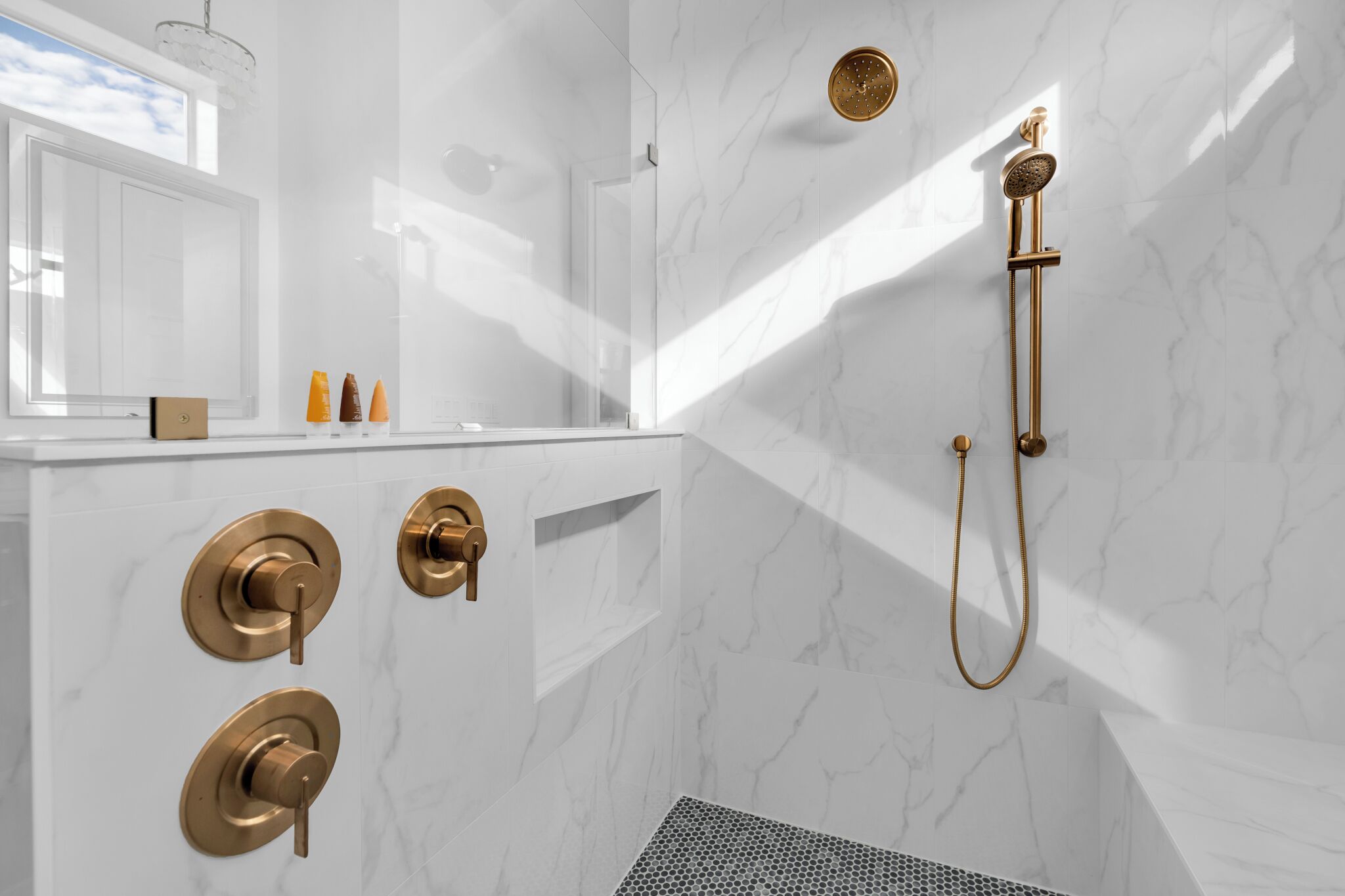 A modern bathroom with a marble wall, a gold showerhead, and a large mirror.