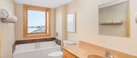Une salle de bain moderne équipée d’une baignoire, de toilettes et d’un lavabo, avec une grande fenêtre et un miroir.