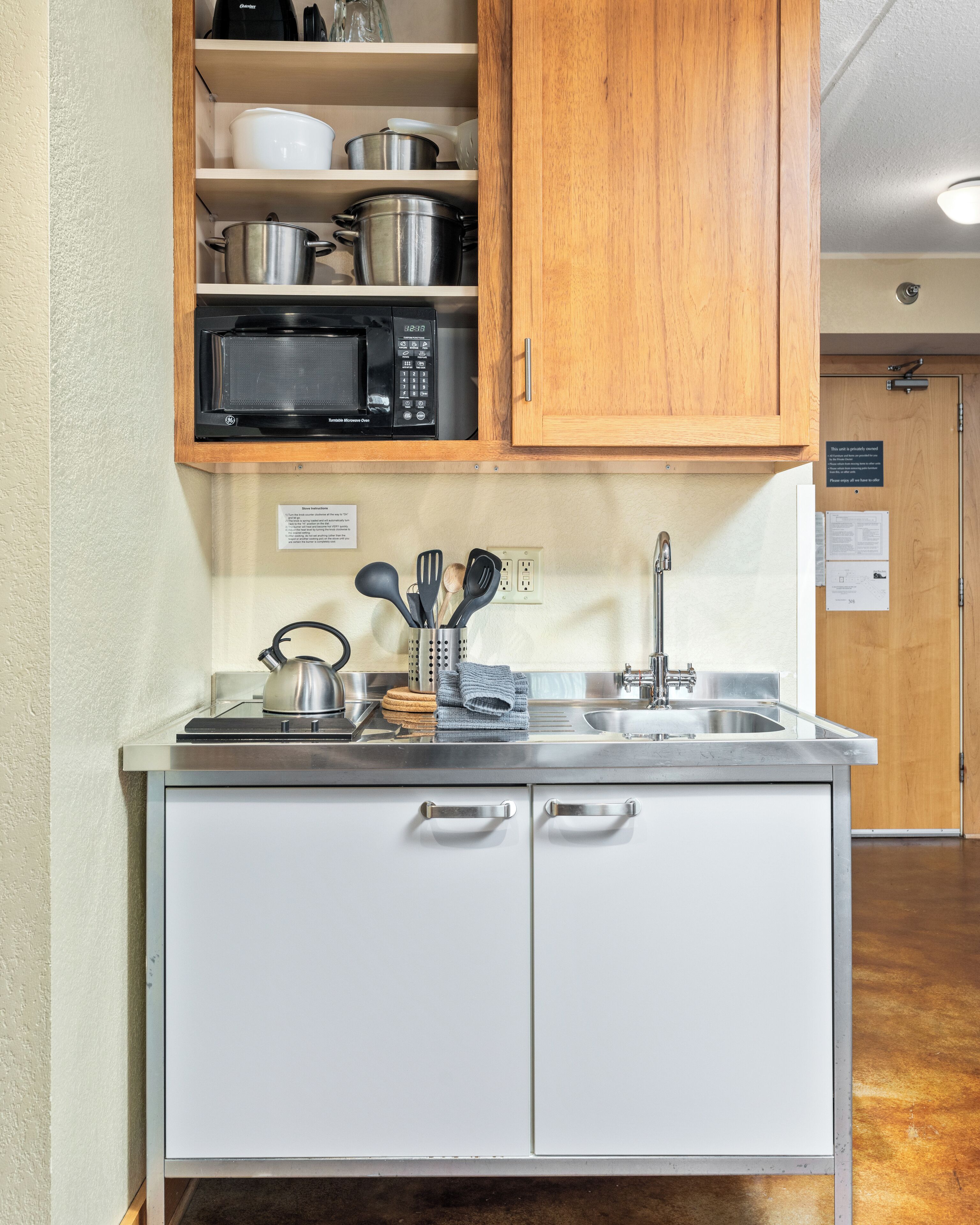 A compact kitchen with a microwave, stainless steel sink, and wooden cabinets.