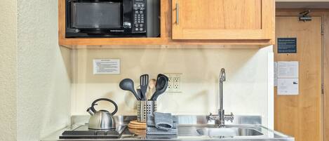 A compact kitchen with a microwave, stainless steel sink, and wooden cabinets.