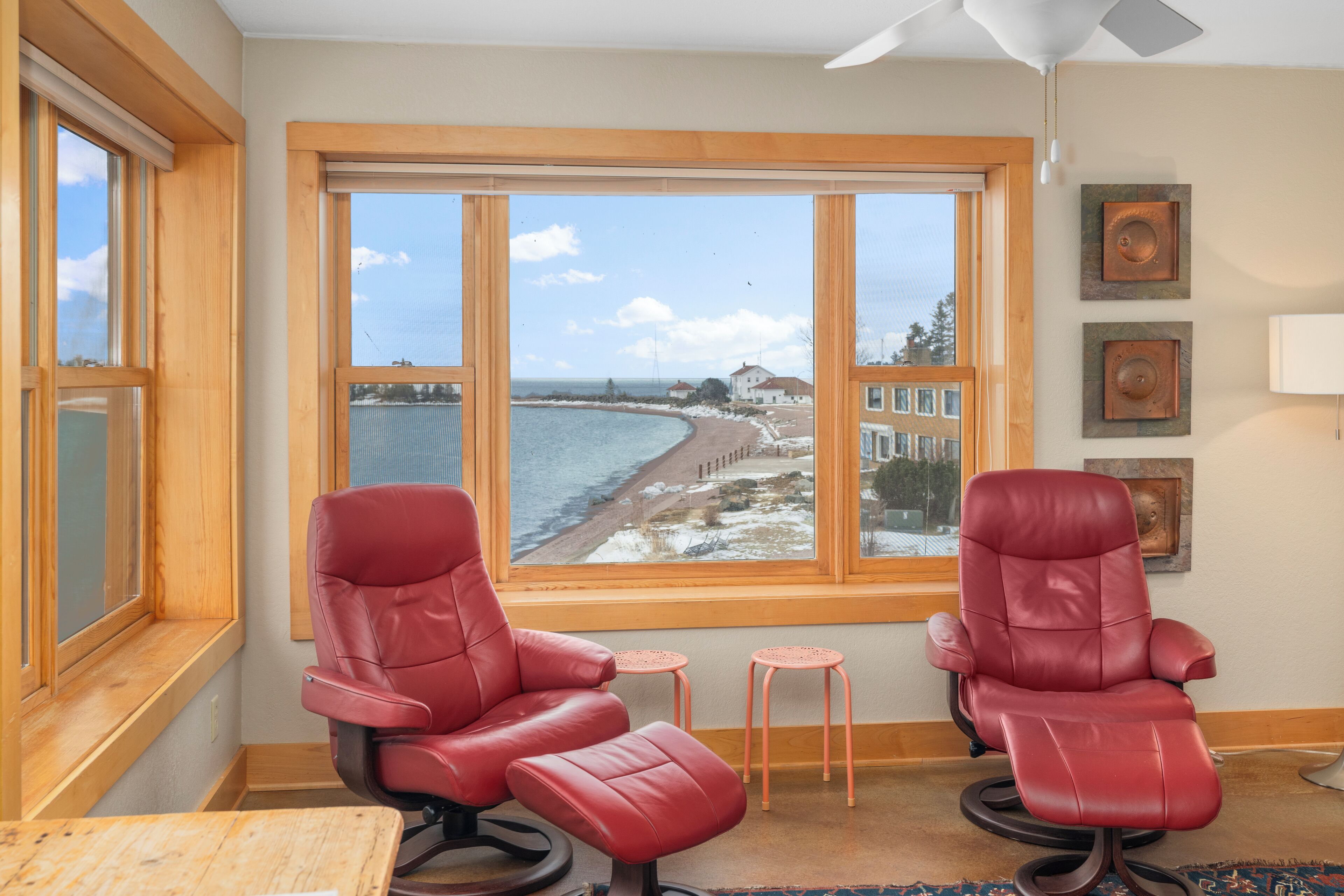 A room with two red leather chairs, a small table, and a view of a beach through large windows.