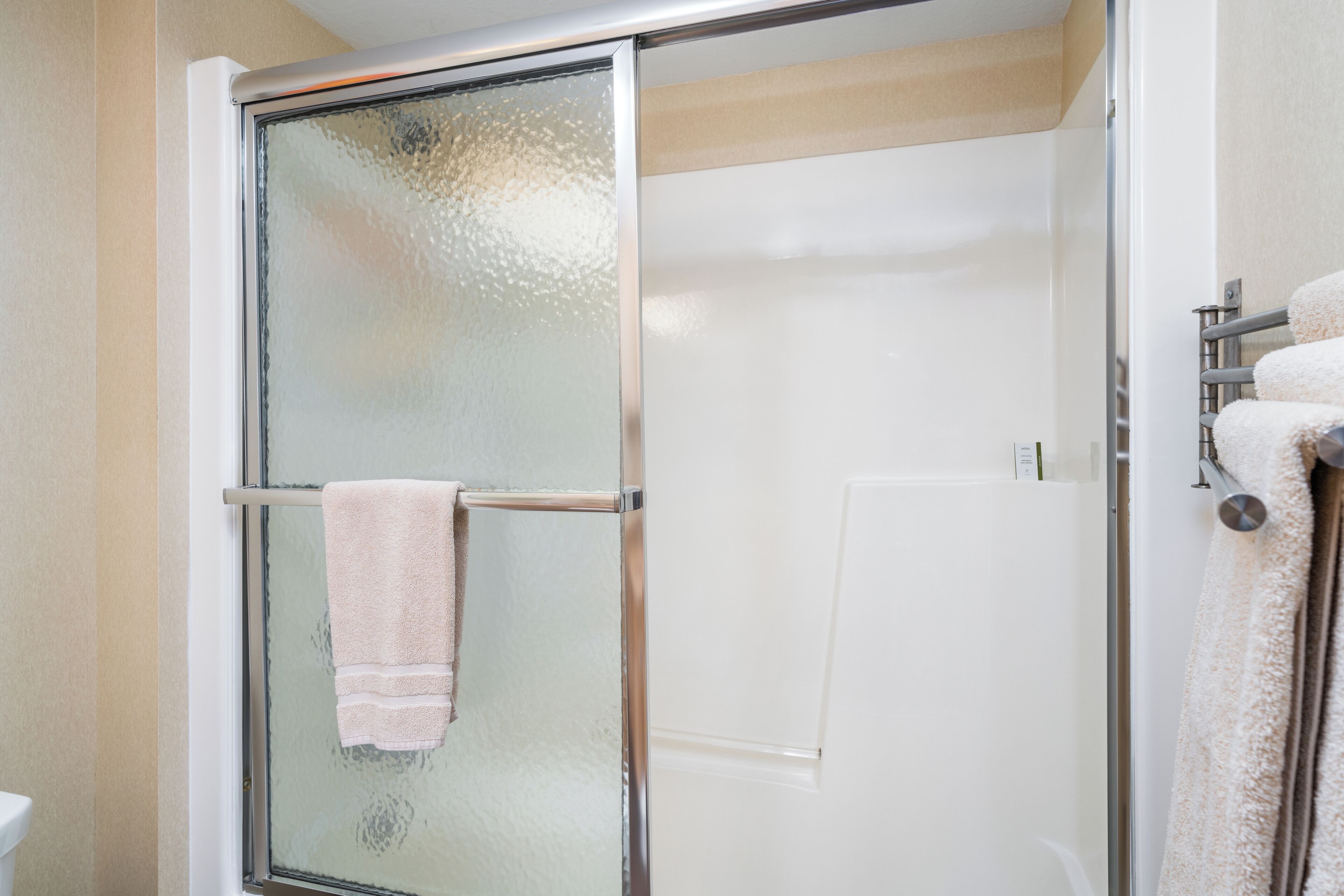 A glass-enclosed shower stall with a towel rack and a white door.