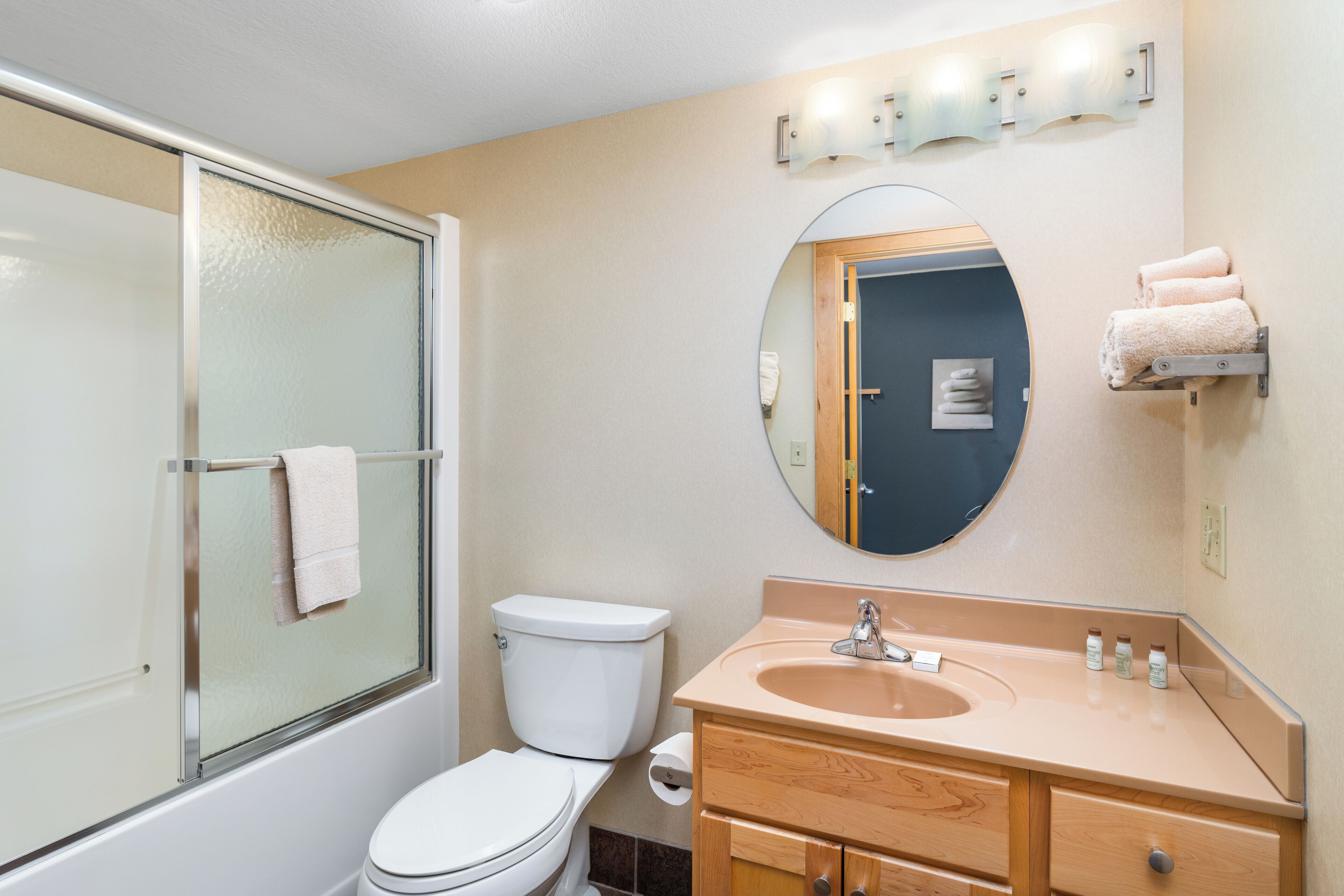 A bathroom with a glass-enclosed shower, a toilet, a sink with a mirror above it, and a towel rack with towels.