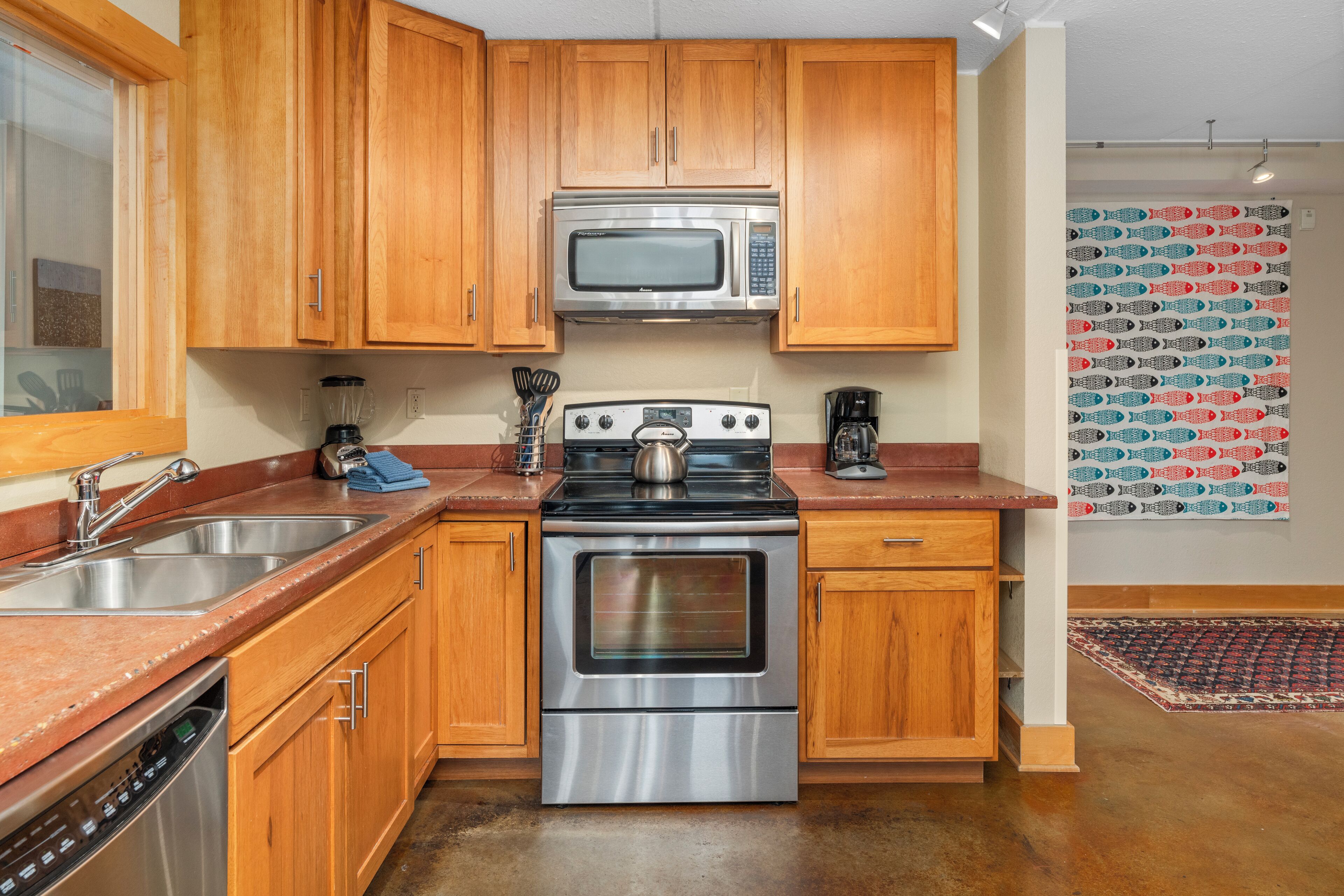 Egy konyha, melyben fa borítású szekrények, rozsdamentes acélból készült háztartási gépek és mintás fal található.