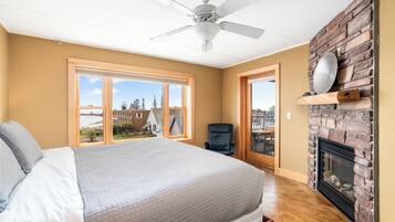 Ein Schlafzimmer mit einem großen Bett, einem Deckenventilator, einem Kamin und Blick ins Freie.