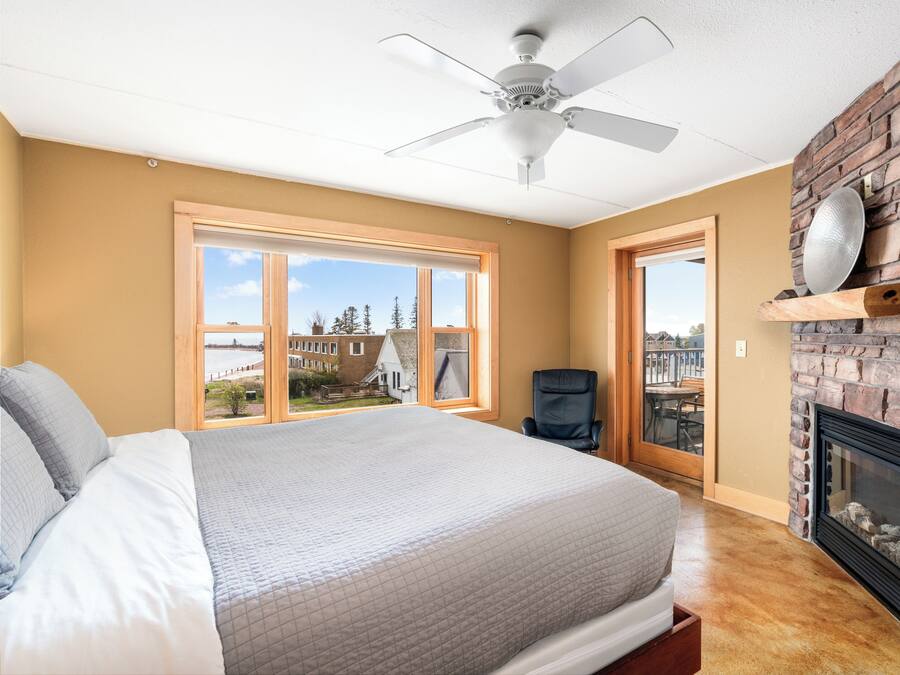 Ein Schlafzimmer mit einem großen Bett, einem Deckenventilator, einem Kamin und Blick ins Freie.