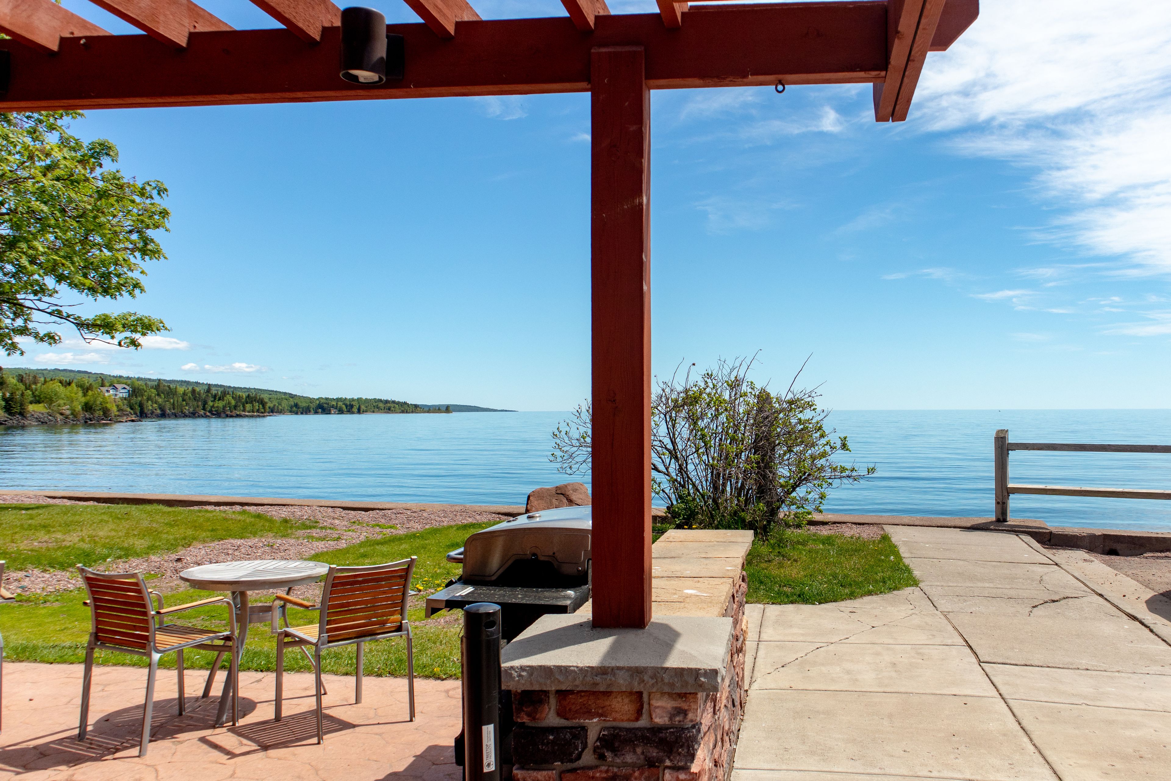 An outdoor patio with a grill, chairs, and a view of a lake.