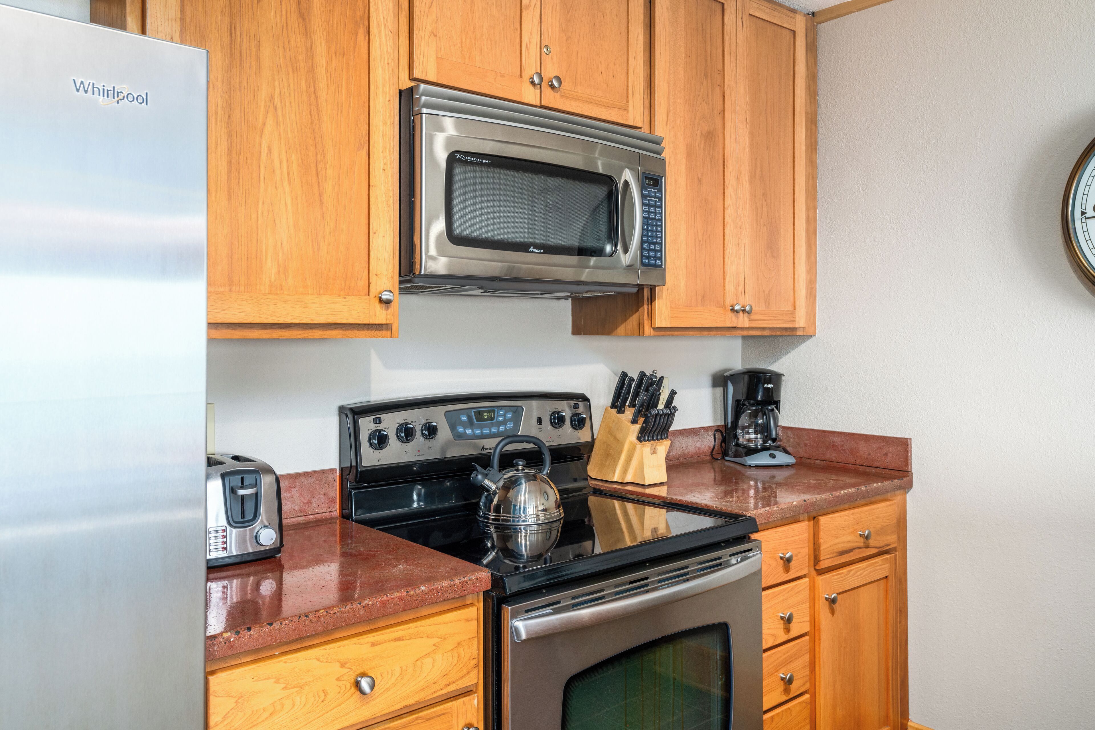 Una cocina compacta con refrigerador de acero inoxidable, microondas, estufa y armarios de madera.