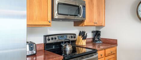 Una cocina compacta con refrigerador de acero inoxidable, microondas, estufa y armarios de madera.