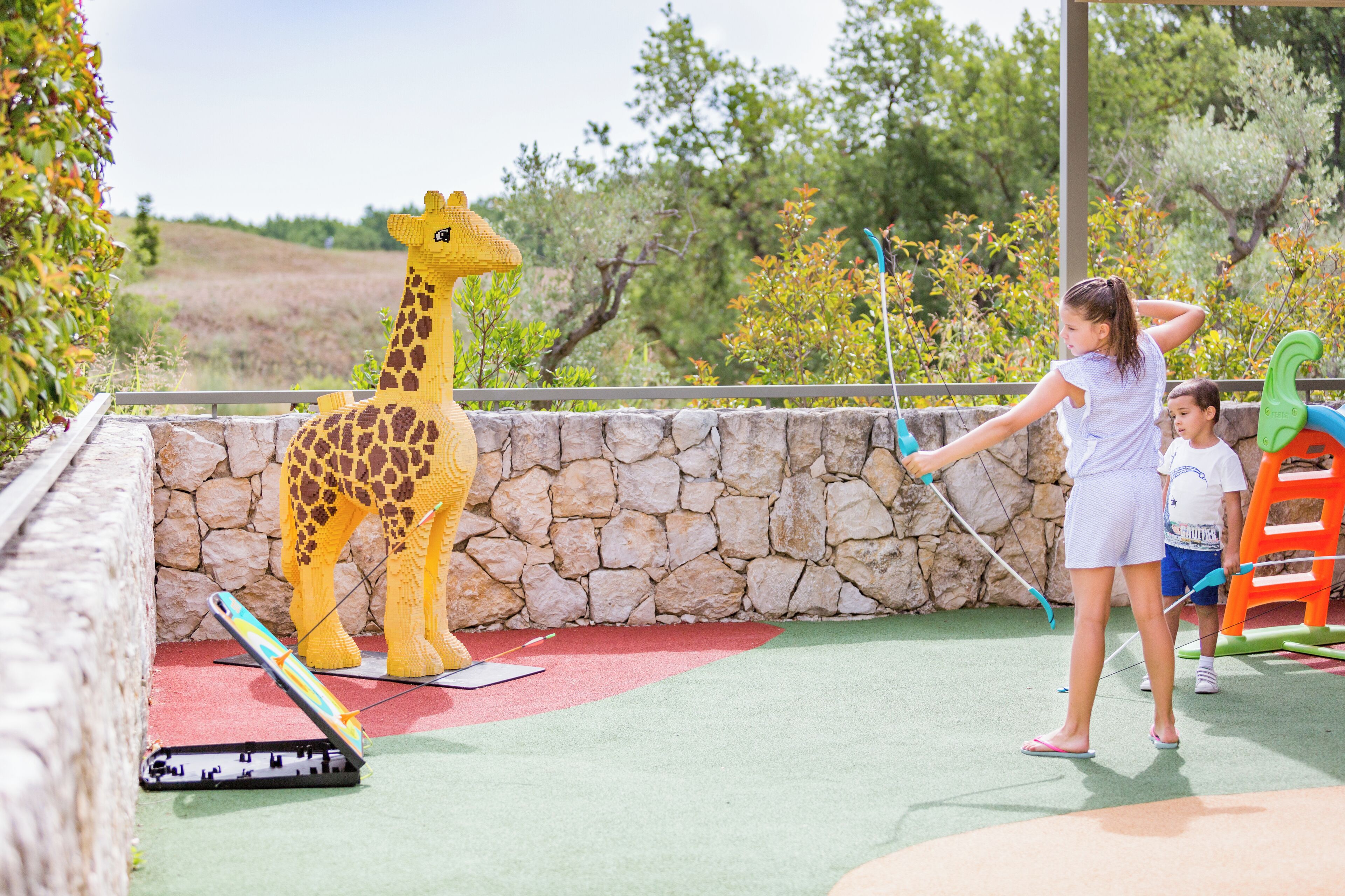 Una estatua de jirafa, un muro de piedra y un niño jugando con un palo de golf de juguete.