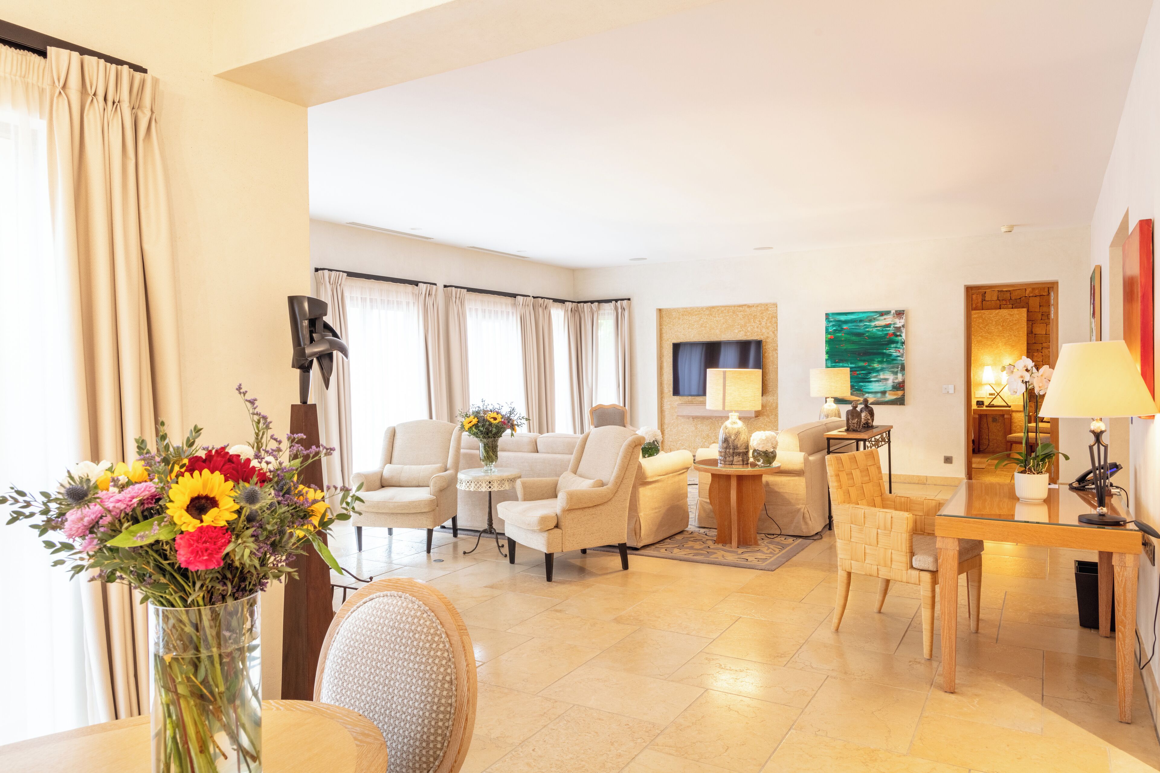 A well-lit living room with a sofa set, a dining table, and a vase of flowers.