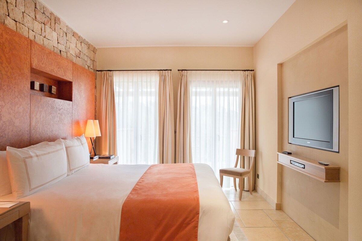 A hotel room with a large bed, a TV mounted on the wall, a chair, and a lamp.