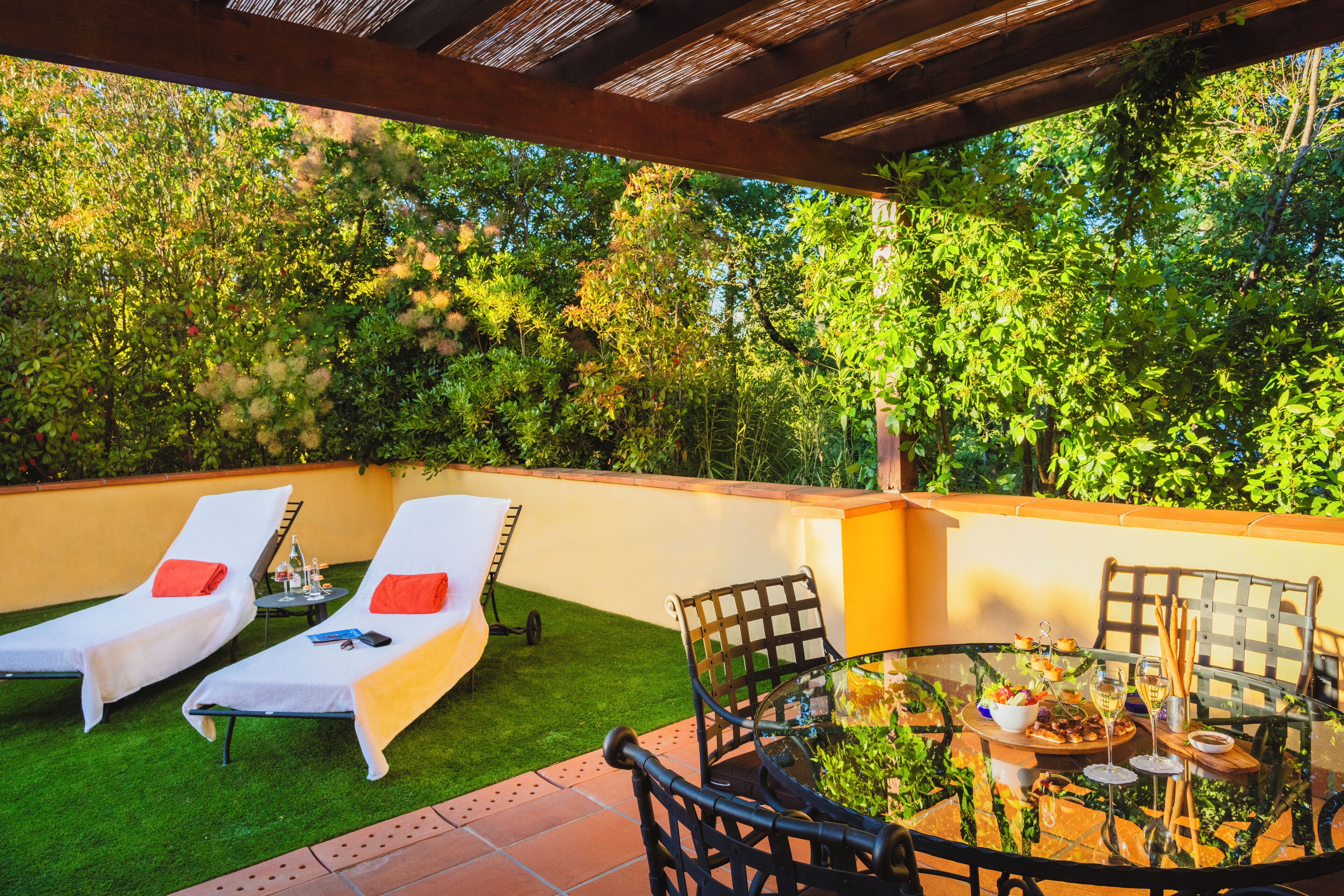 Un patio con dos tumbonas, una mesa redonda con sillas y un pequeño jardín.