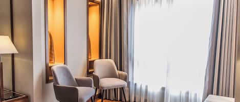 Habitación de hotel con dos sillones, una mesita, una lámpara y un ventanal con cortinas.