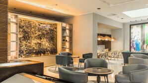Un moderno vestíbulo de hotel con pared de mármol, zona de estar y un amplio ventanal con una obra de arte.