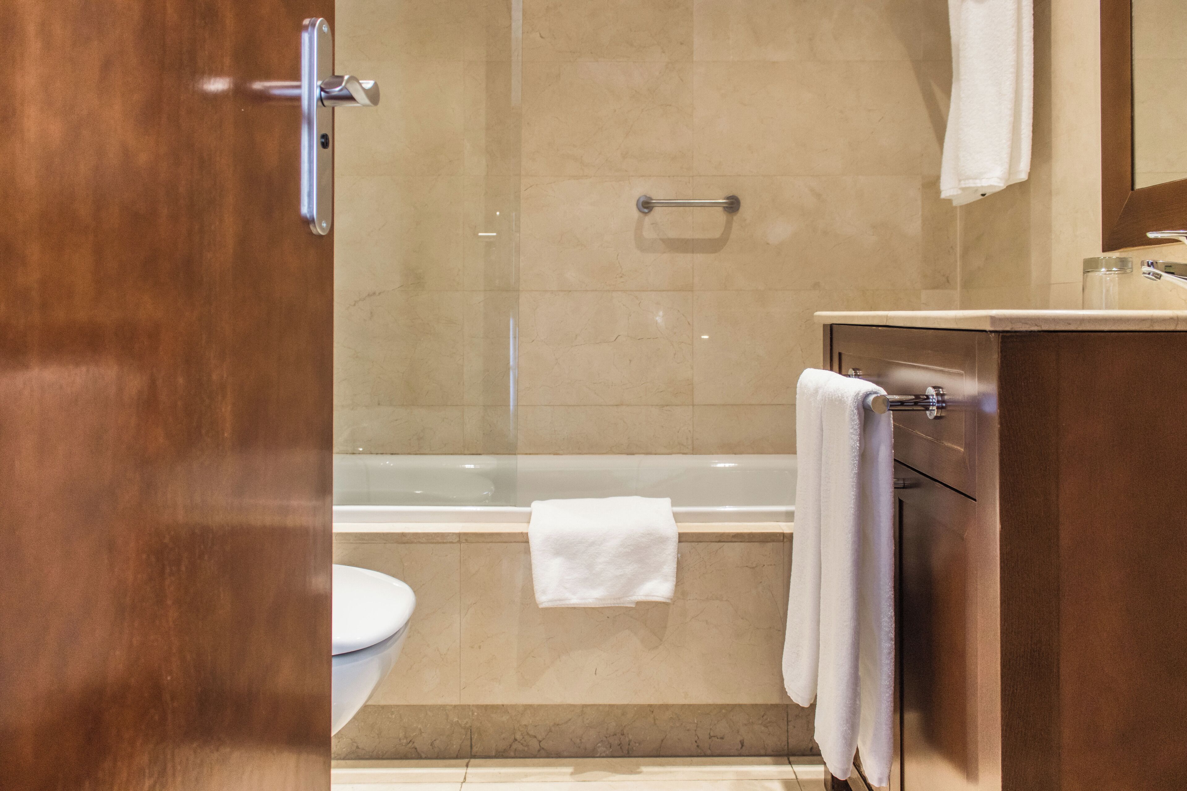Une salle de bain moderne avec une douche à parois de verre, des toilettes blanches et un meuble-lavabo en bois, avec une serviette suspendue sur le côté.
