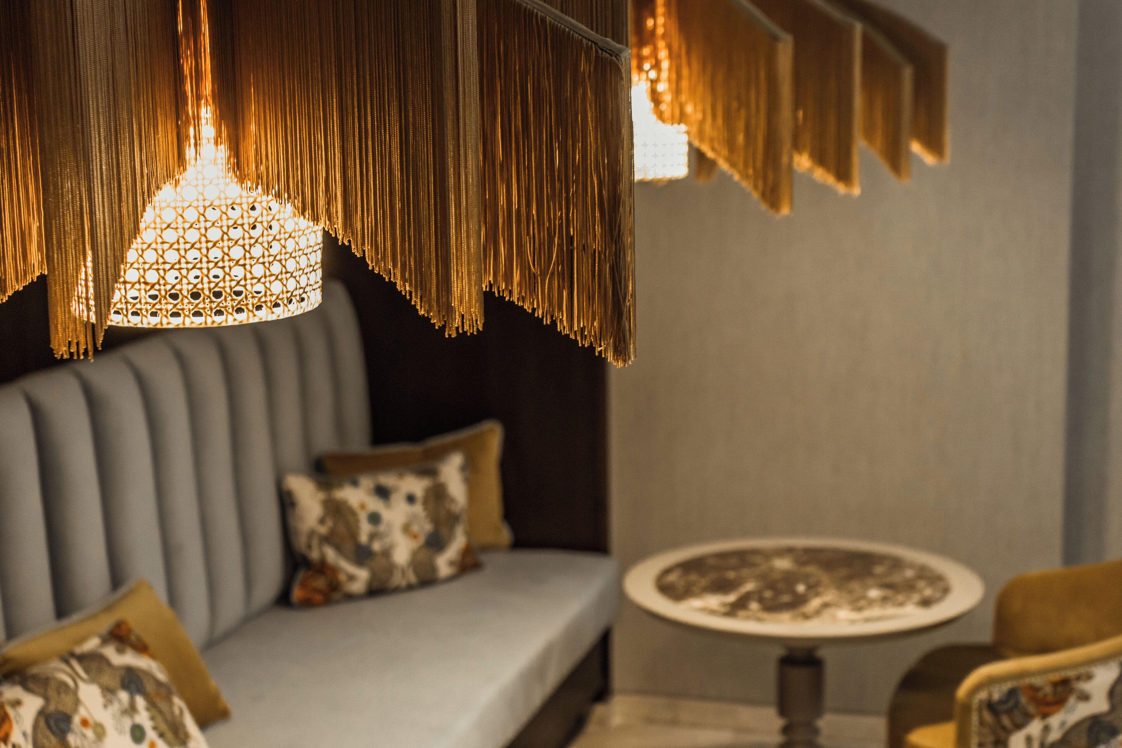 Un salon moderne avec un canapé gris, des coussins à motifs, une table basse ronde et un luminaire suspendu.