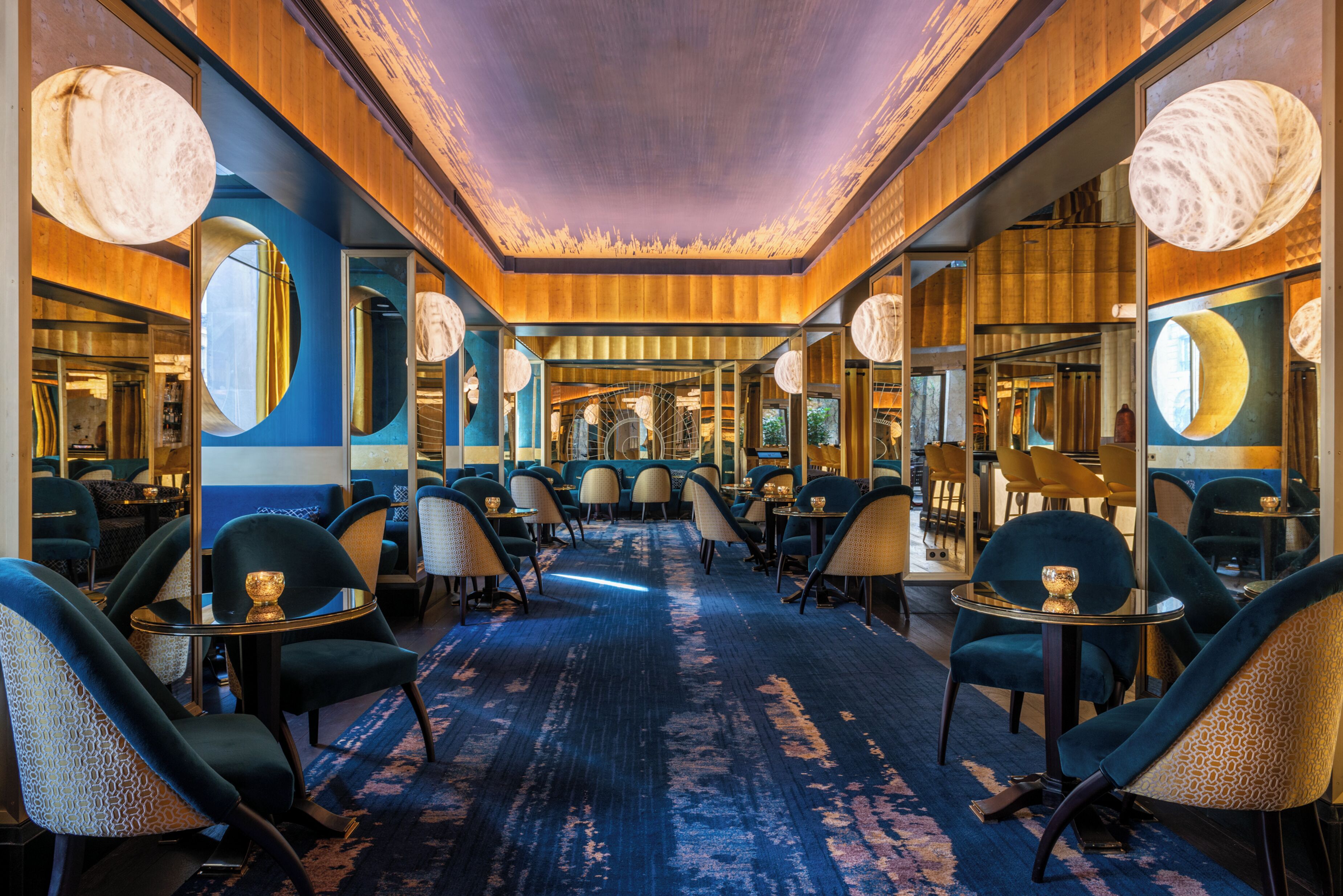 A hotel lobby with a central carpeted walkway, mirrored walls, and round tables with chairs.