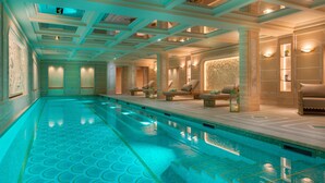 A large indoor swimming pool with a tiled floor, surrounded by lounge areas with seating and decorative lighting.