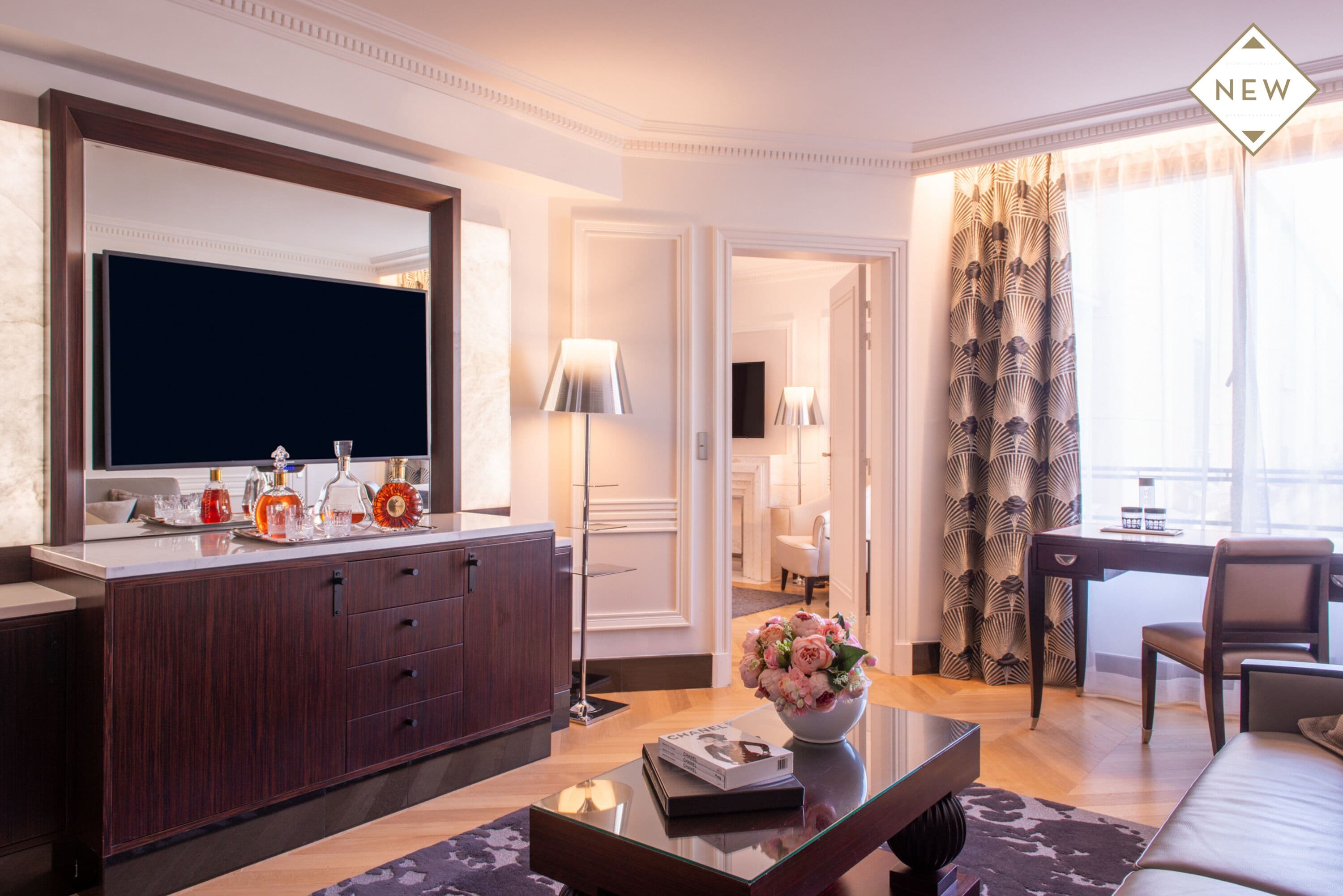 Una sala moderna con un televisor de pantalla plana grande, un mueble de madera oscura y una mesa de centro de vidrio con una revista y un jarrón de flores.