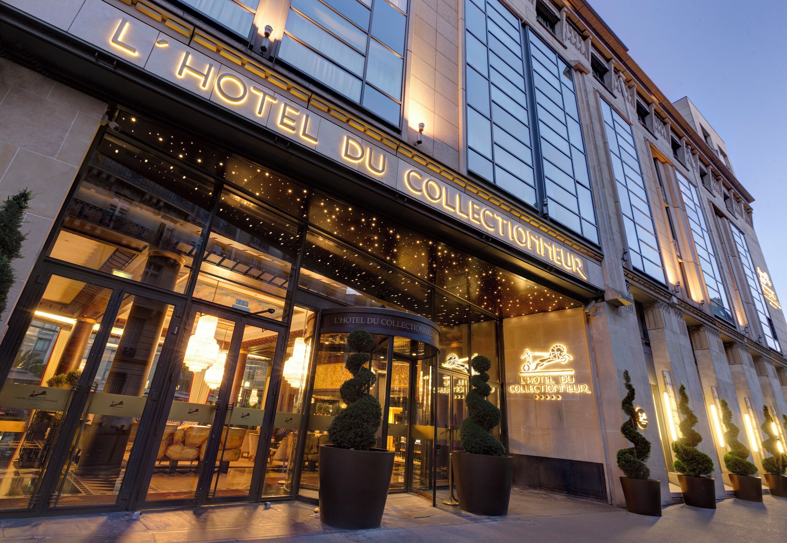 Das Außere von L'Hotel Du Collectionneur mit beleuchteter Beschilderung und einer modernen Fassade.