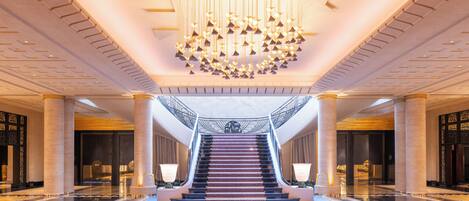 A grand lobby with a central staircase, large columns, and a chandelier.