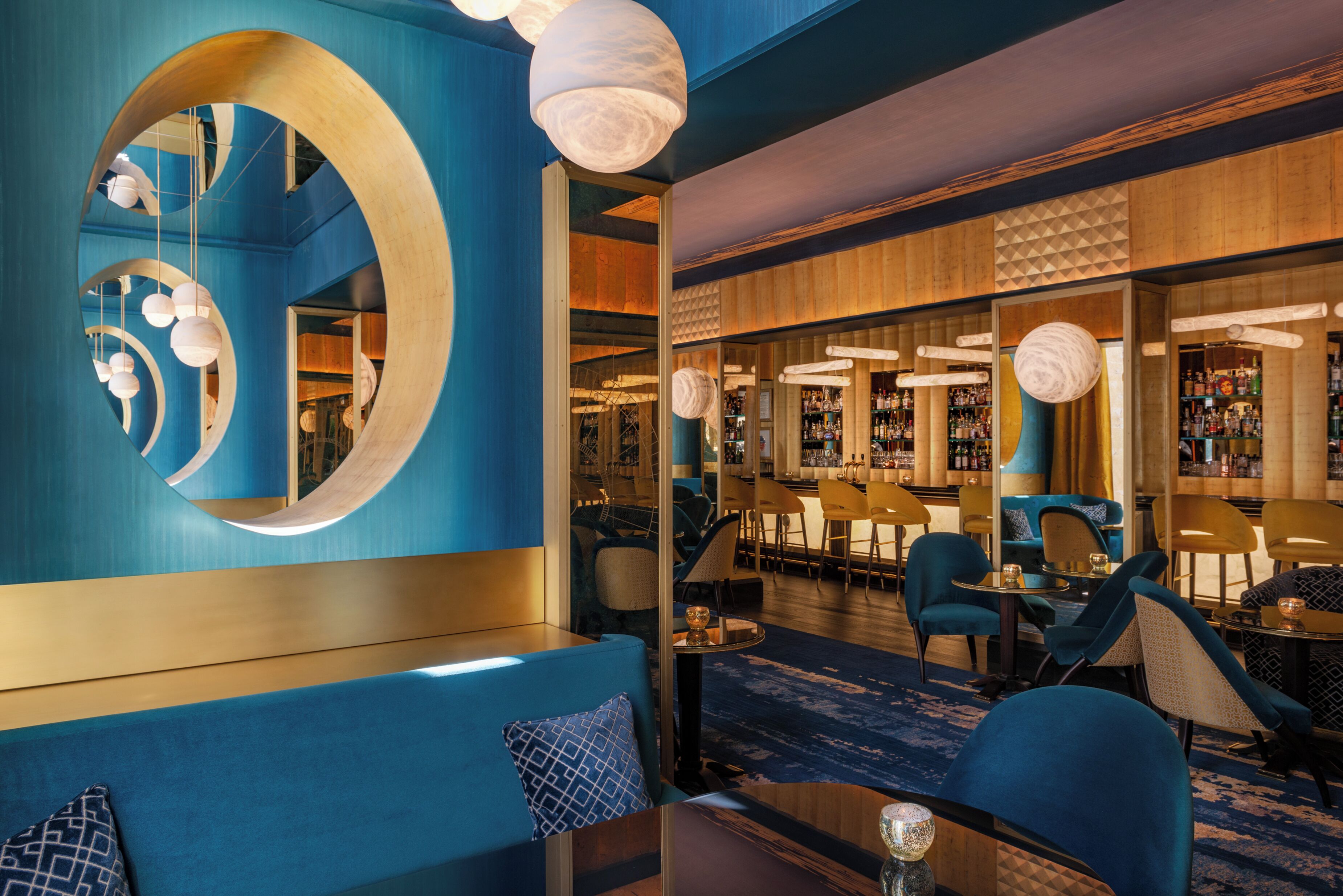 A modern bar area with blue seating, a large mirror, and hanging spherical light fixtures.
