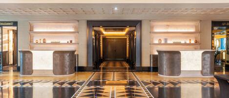 A hotel lobby with a geometric patterned floor, a reception desk, and shelves with decorative items.