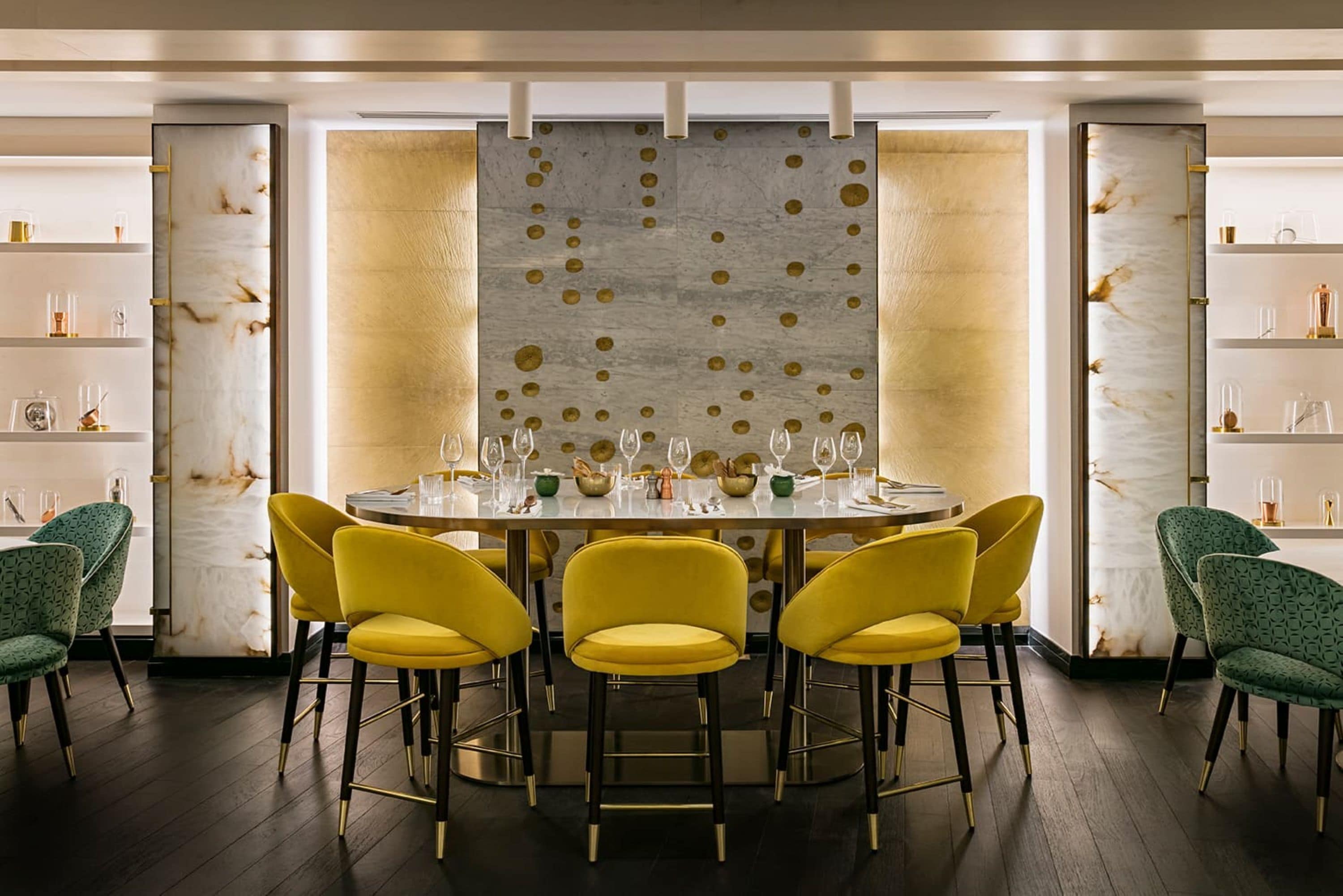 A modern dining area with a round table, yellow chairs, and a decorative wall with circular patterns.