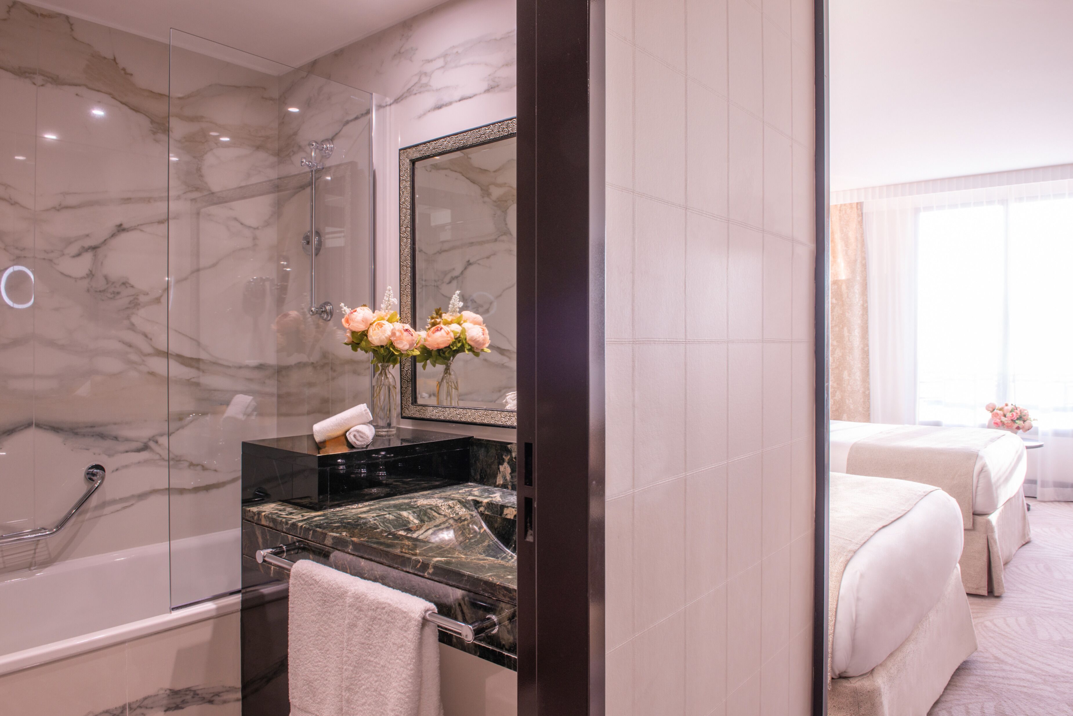 A hotel bathroom with a marble shower, a black sink, and a mirror.