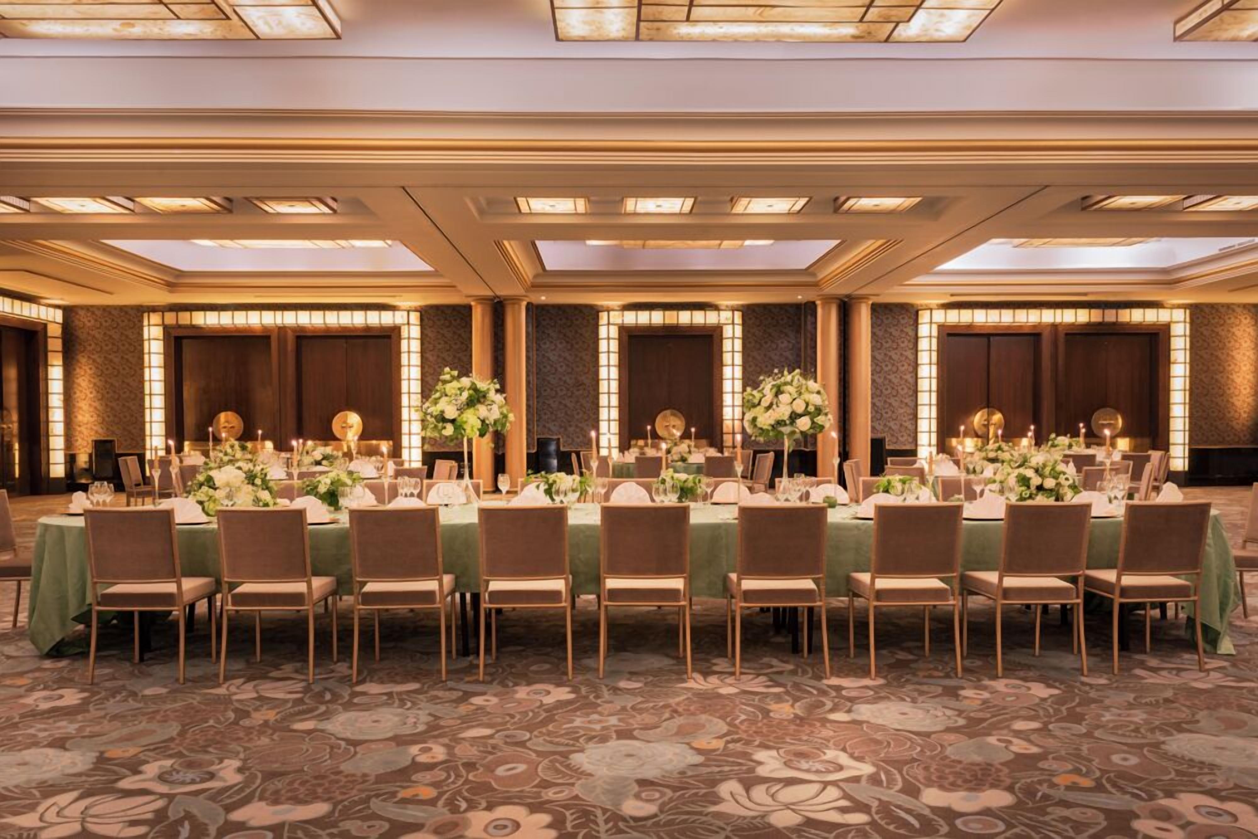 Un salón de banquetes con largas mesas dispuestas para un evento formal, con centros de mesa florales e iluminación con velas.