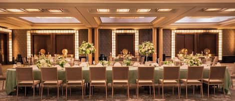 Un salón de banquetes con largas mesas dispuestas para un evento formal, con centros de mesa florales e iluminación con velas.