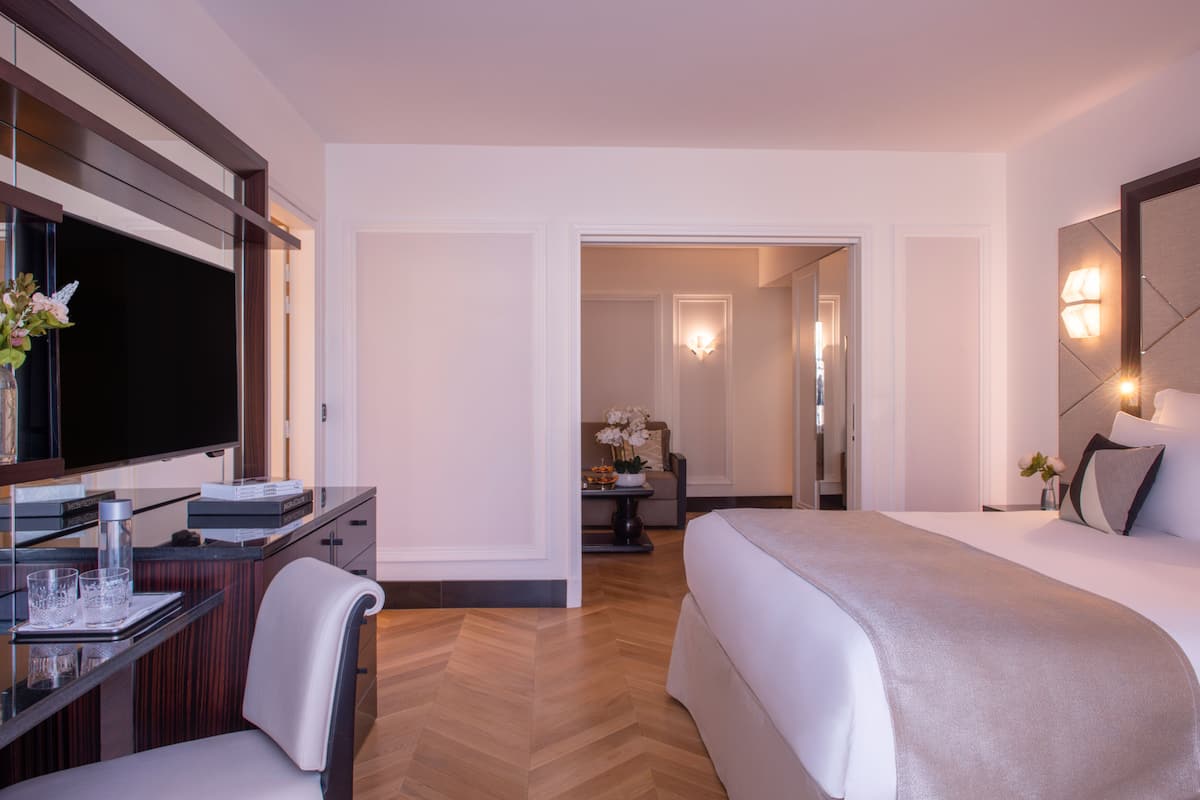 Una habitación de hotel moderna con una cama grande, un escritorio con televisión de pantalla plana, una silla y una mesita con un jarrón de flores.
