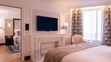 Een moderne hotelkamer met een groot bed, een flatscreen televisie boven een open haard, een spiegel en uitzicht op de stad door grote ramen.