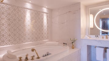 A modern bathroom with a freestanding bathtub, a large mirror with a circular light, and a marble wall.