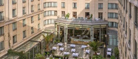A hotel courtyard with a central glass-roofed dining area, surrounded by neatly arranged outdoor seating and a well-maintained lawn.
