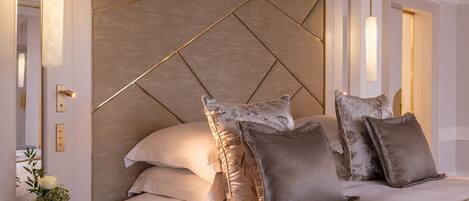 A modern hotel room with a geometric-patterned headboard, a bedside table with a vase of flowers, and a neatly made bed with multiple pillows.