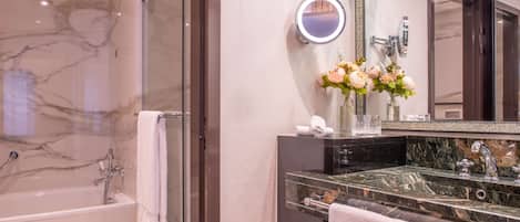 Un baño moderno con ducha acristalada, pared de azulejos de mármol, tocador con espejo y un jarrón de flores.