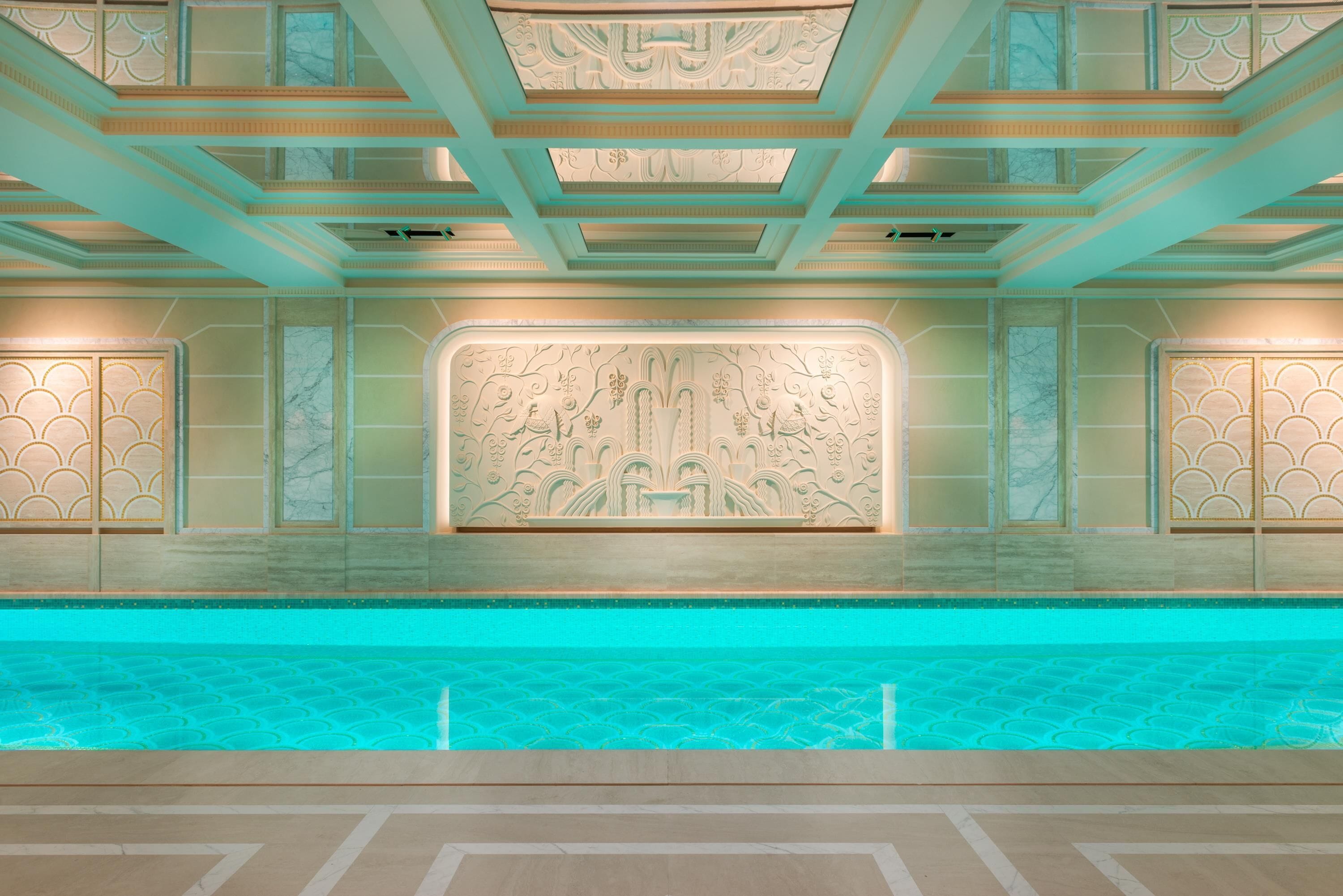 A luxurious indoor pool area with a geometric floor pattern, a decorative wall with intricate designs, and a ceiling with a grid-like structure.