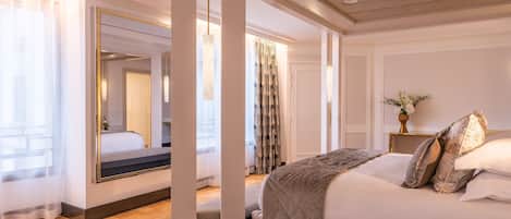 A spacious bedroom with a large bed, a mirror, and a view of the hallway.
