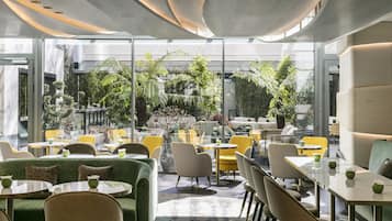 Un jardin intérieur moderne, doté d’espaces aménagés pour s’asseoir, de murs en verre et de nombreuses plantes.