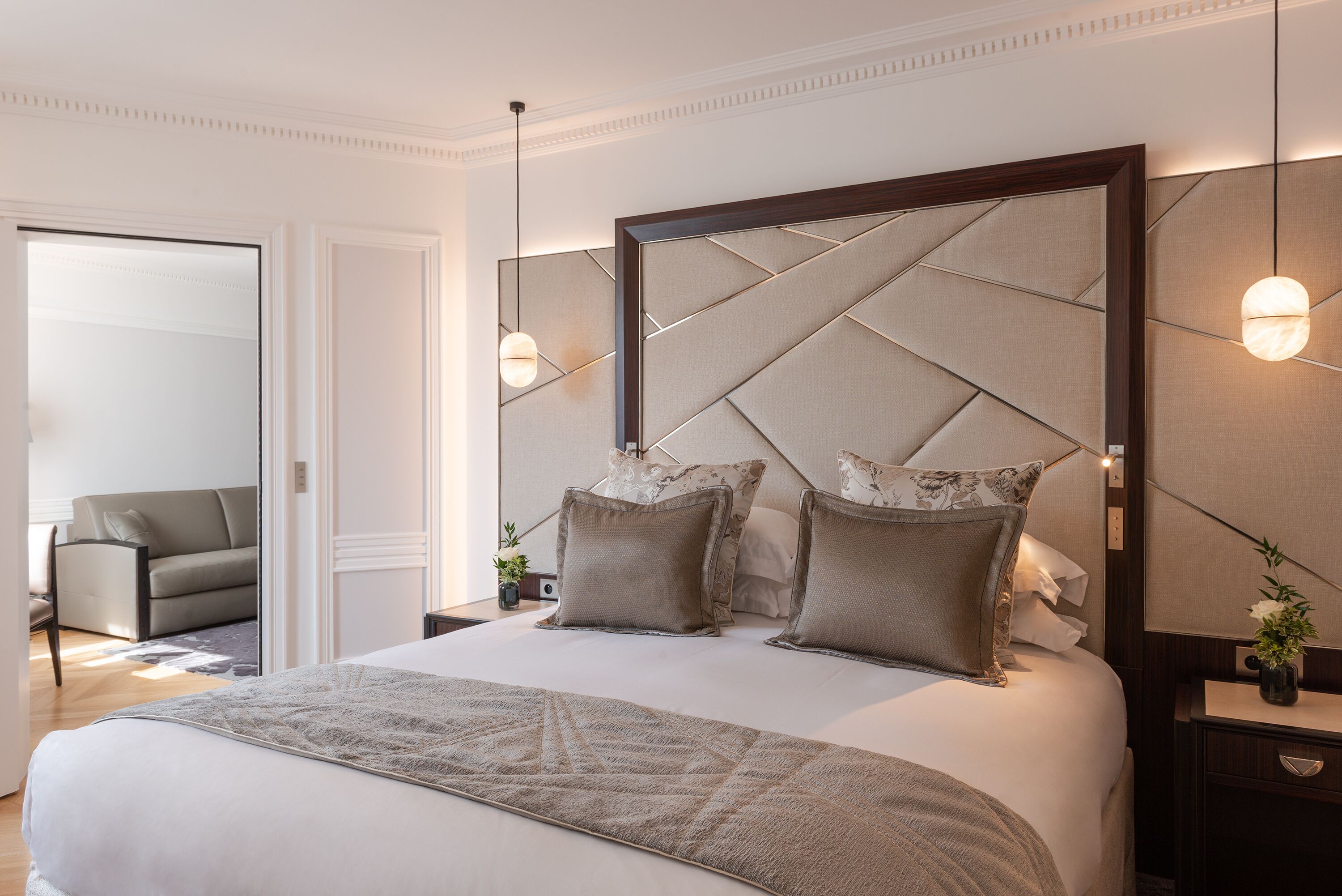 Une chambre à coucher bien rangée, avec un grand lit, une table de chevet avec une lampe et une chaise au fond de la pièce.